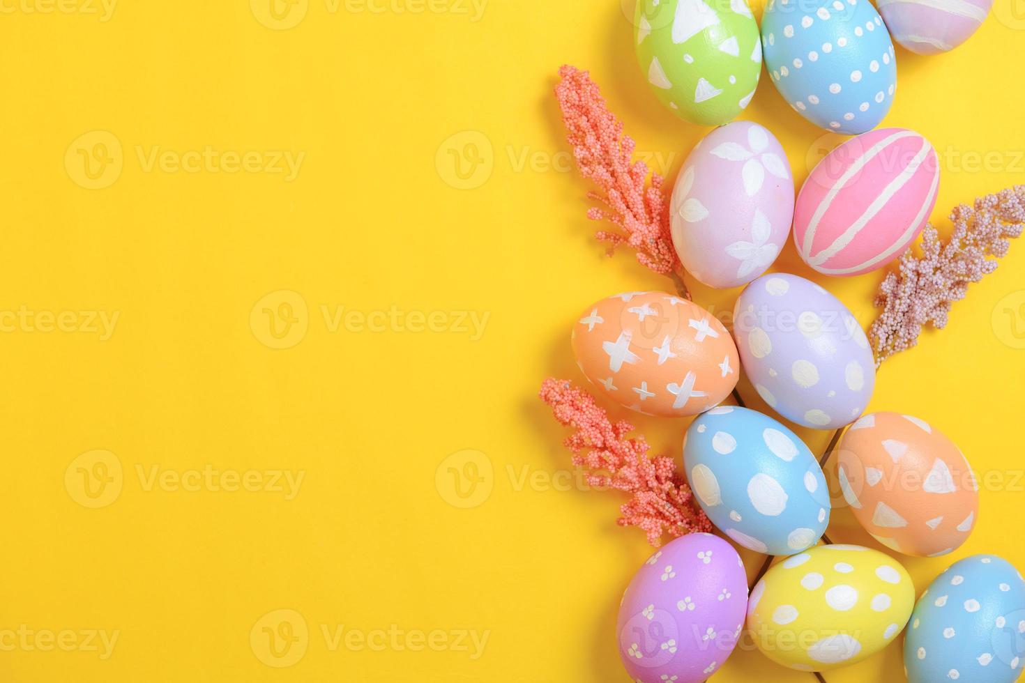 Happy Easter holiday greeting card design concept. Colorful Easter Eggs and spring flowers on yellow background. Flat lay, top view, copy space. photo