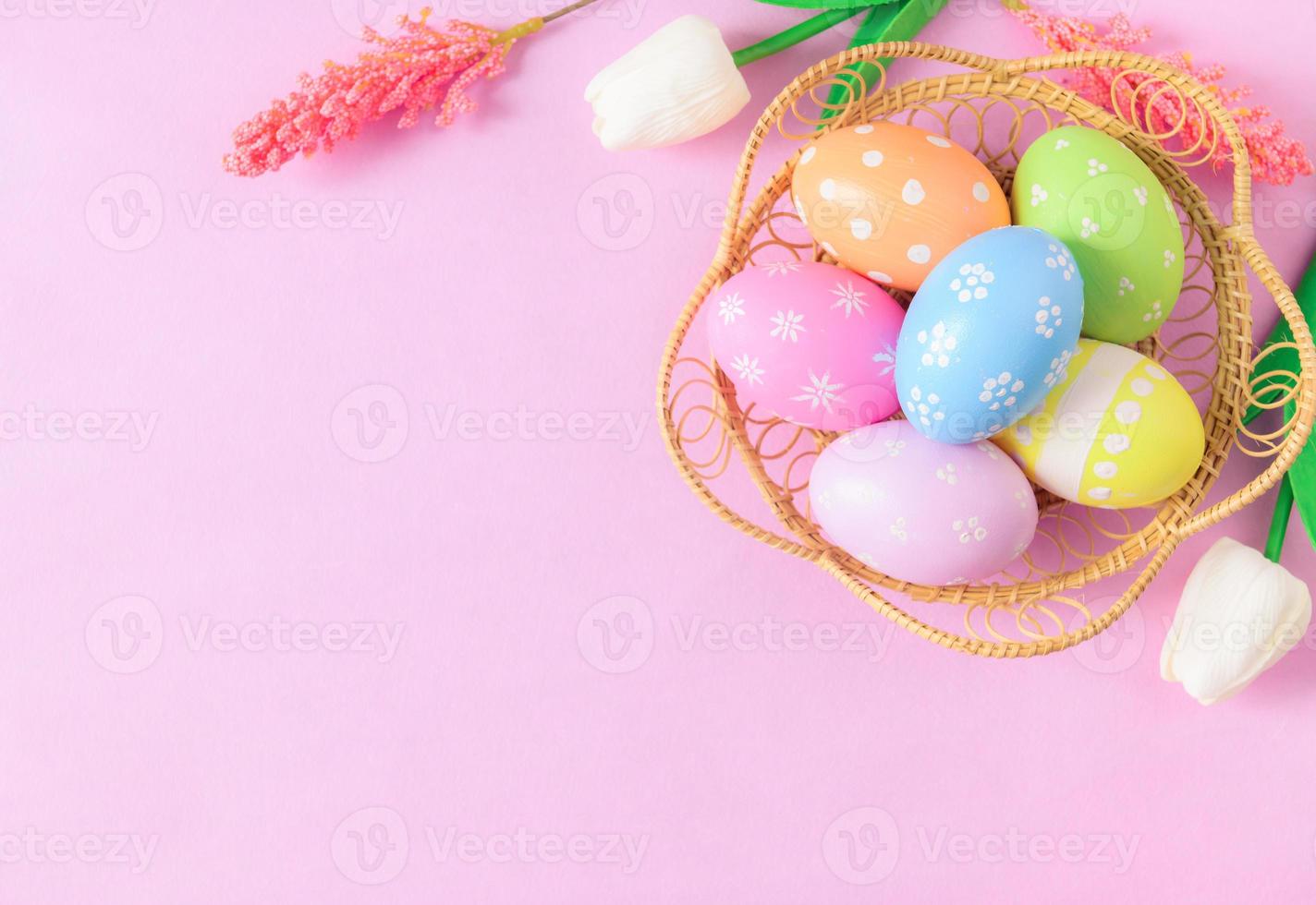 Happy Easter holiday greeting card concept. Colorful Easter Eggs and spring flowers on pastel pink background. Flat lay, top view, copy space. photo