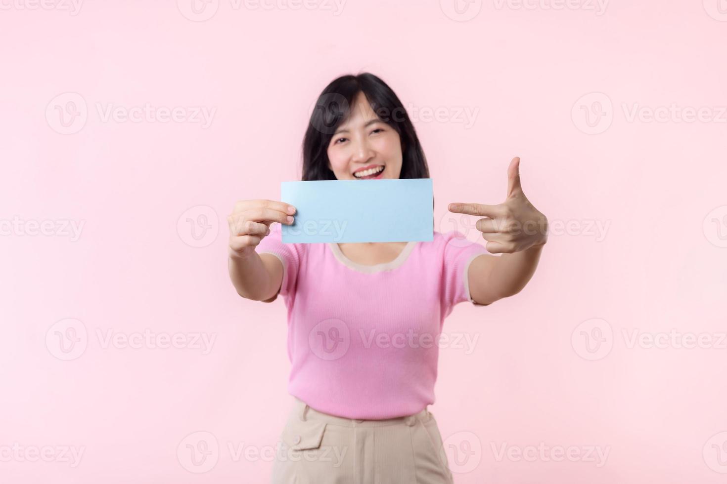 Portrait happy young woman model holding and showing blank space paper for advertisement information message poster with thumb up or point finger gesture isolated on pink pastel studio background. photo