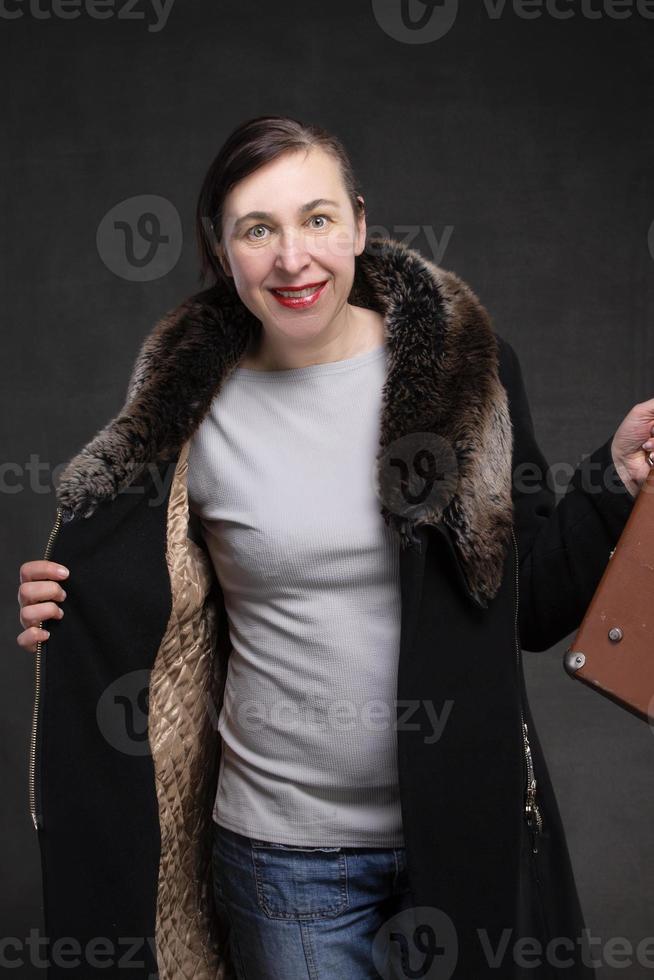 Happy fifty year old woman in a coat with a fur collar on a gray background. Portrait of a middle-aged woman. photo