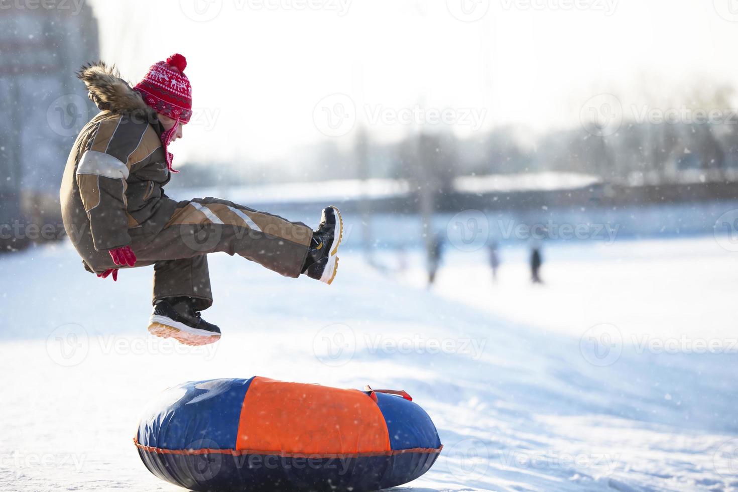 Little child on a sleigh. Child on a winter day. A boy is riding on a snow slide. photo