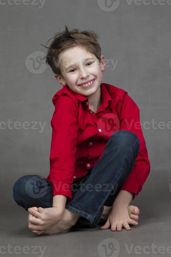 Portrait of a happy little boy in a red shirt and jeans on a gray background. Child of ten. photo