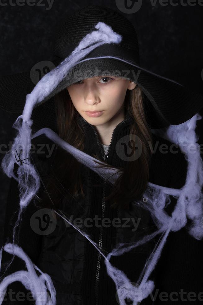 pequeño niña en un negro sombrero en un Víspera de Todos los Santos araña web. foto