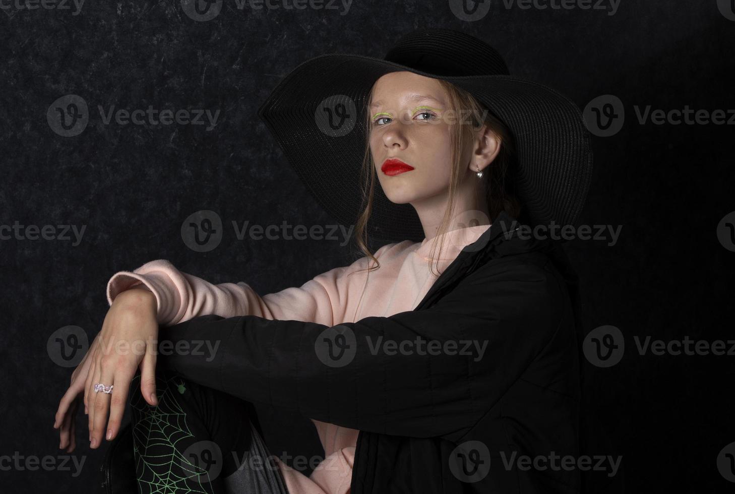 A teenage girl in a black hat dressed up for the holiday of halloween. photo