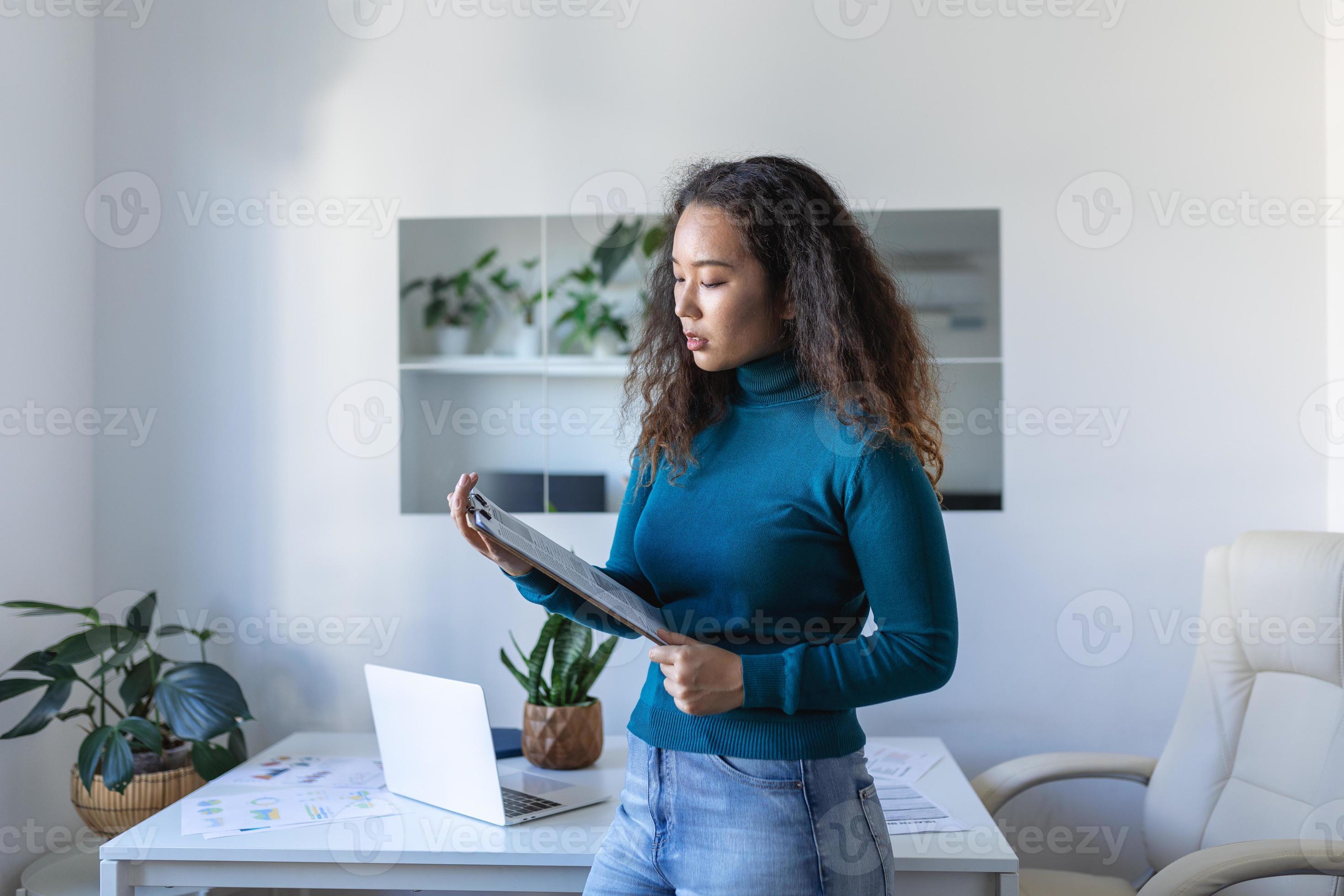 Smiling young Asian female employee stand at desk in office look in