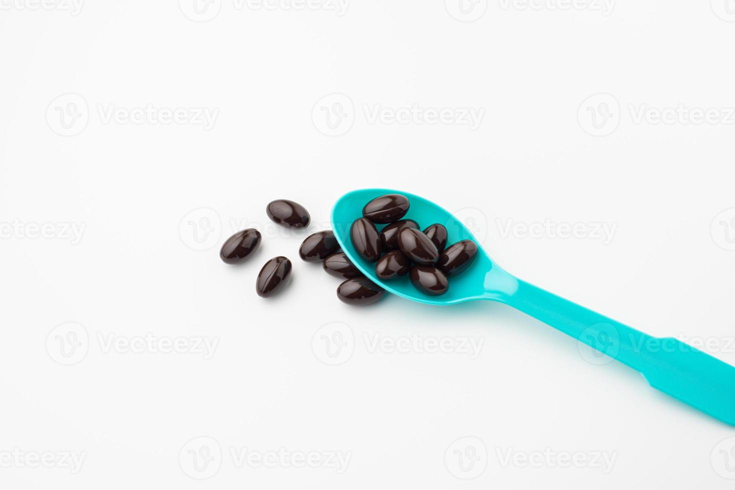Black soft gel capsules in a blue spoon on a white background. Vitamin food supplements photo