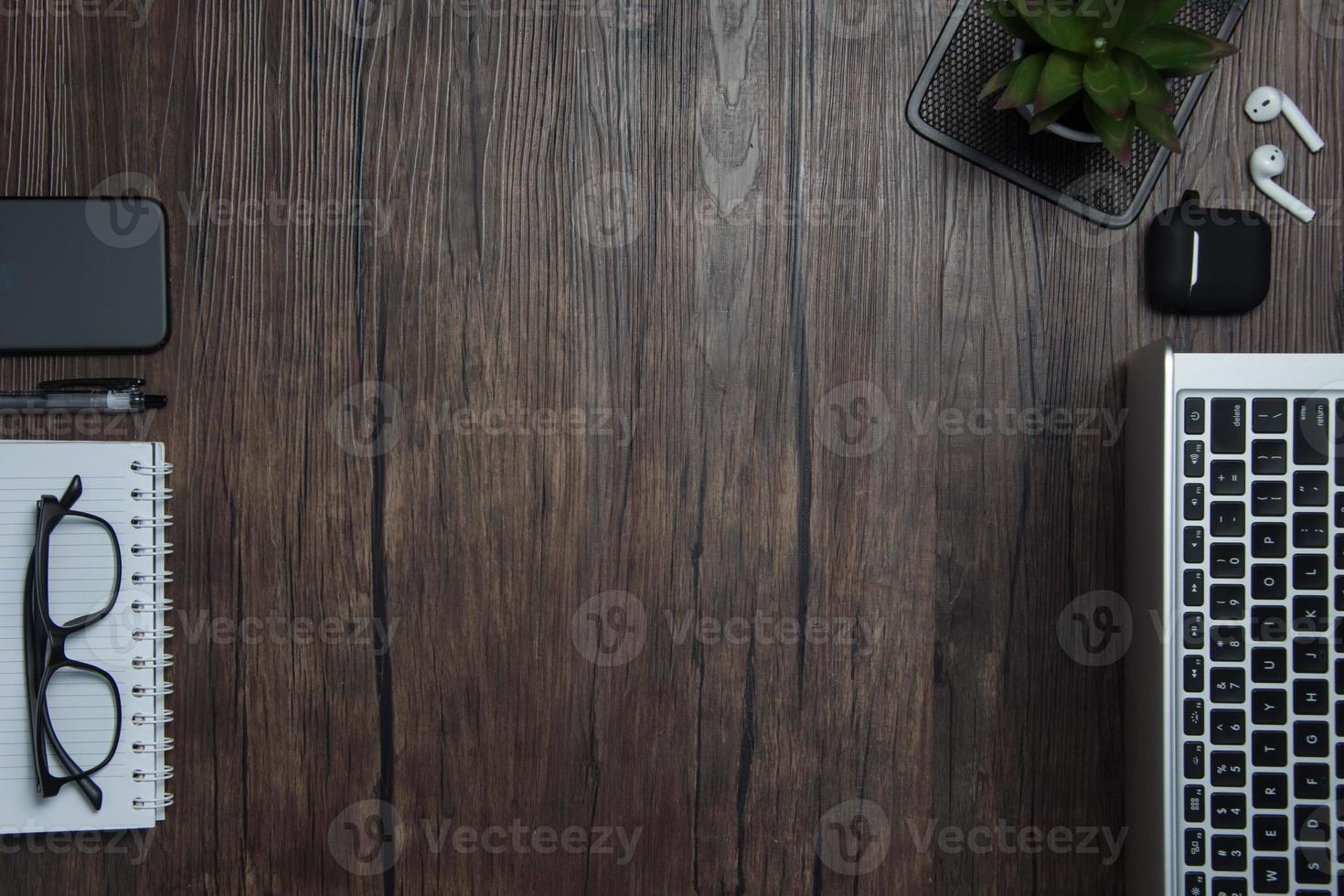 wooden office desk with laptop, blank notebook, cordless earphones and glasses, dark background, wooden background, Top view with copy space, empty space. photo