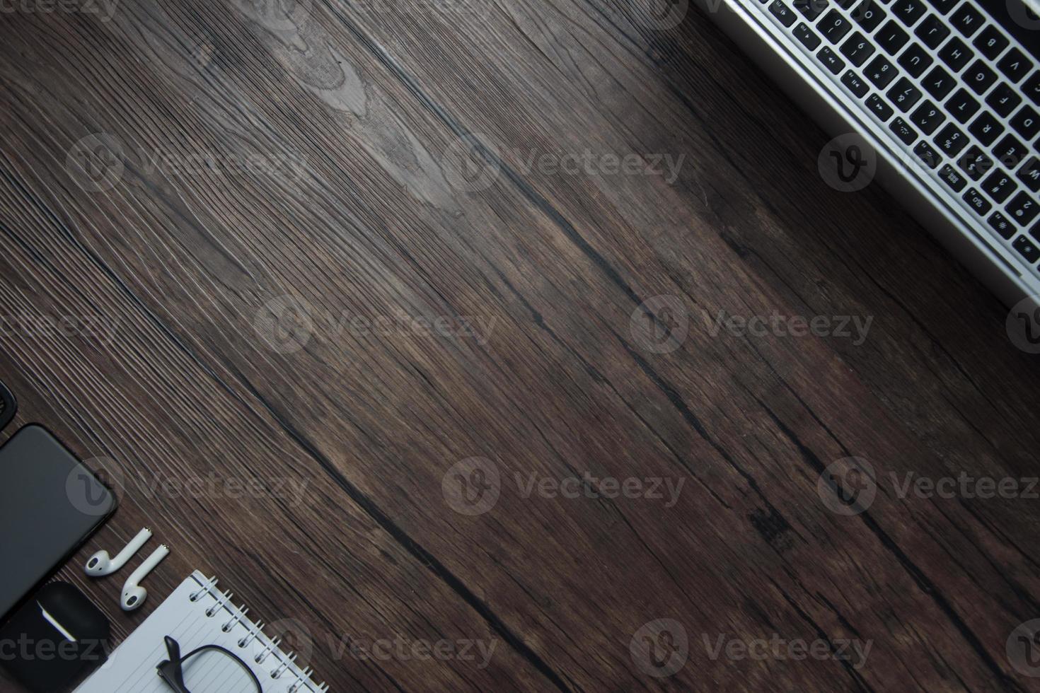 wooden office desk with laptop, blank notebook, cordless earphones and glasses, dark background, wooden background, Top view with copy space, empty space. photo