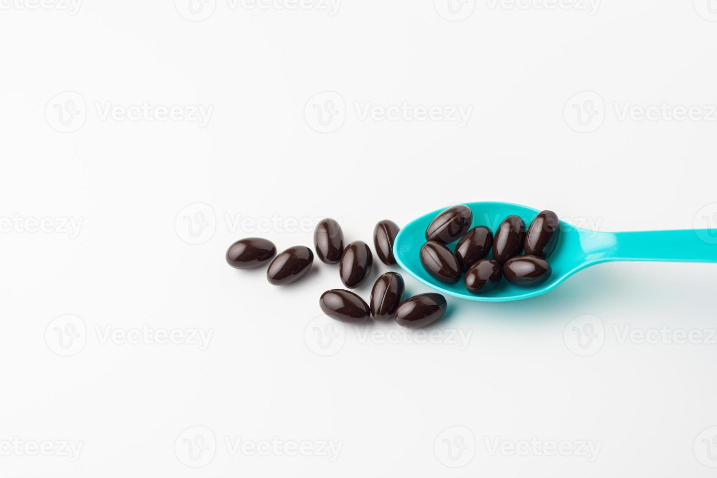 Black soft gel capsules in a blue spoon on a white background. Vitamin food supplements photo