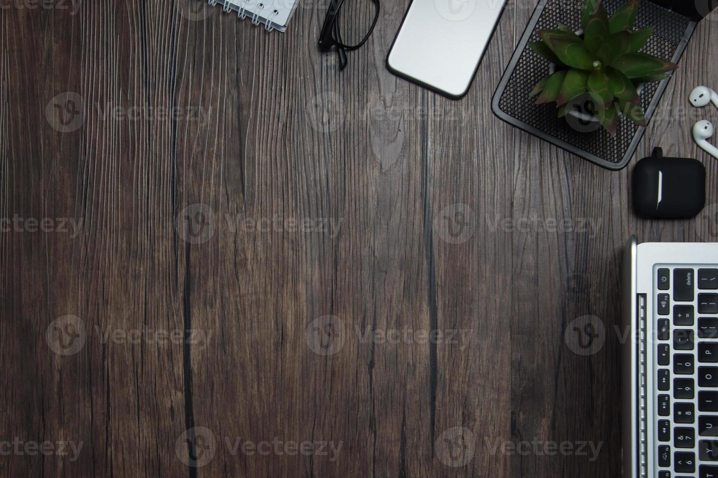 wooden office desk with laptop, blank notebook, cordless earphones and glasses, dark background, wooden background, Top view with copy space, empty space. photo