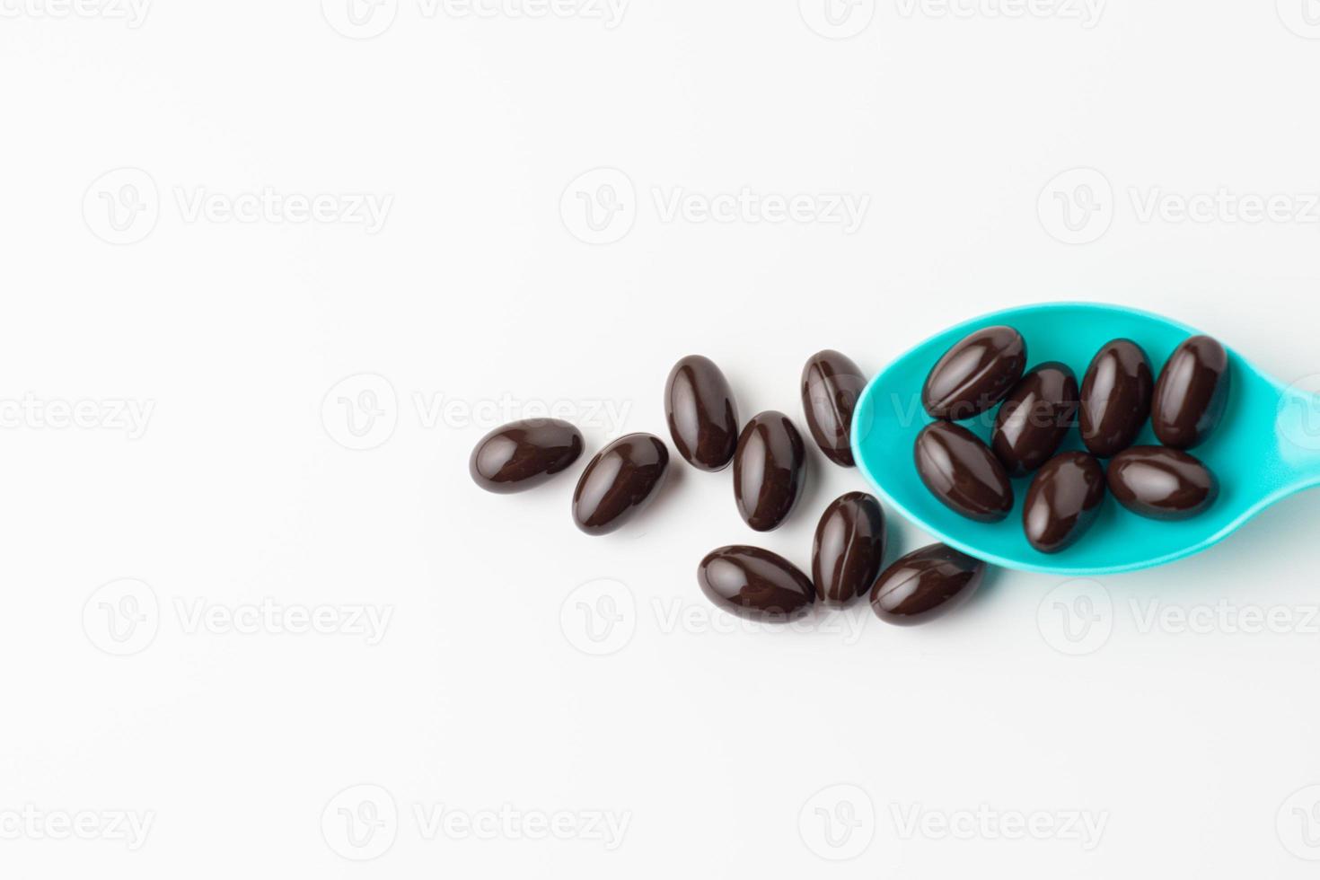 Black soft gel capsules in a blue spoon on a white background. Vitamin food supplements photo