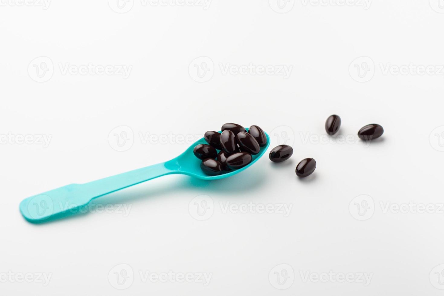 Black soft gel capsules in a blue spoon on a white background. Vitamin food supplements photo