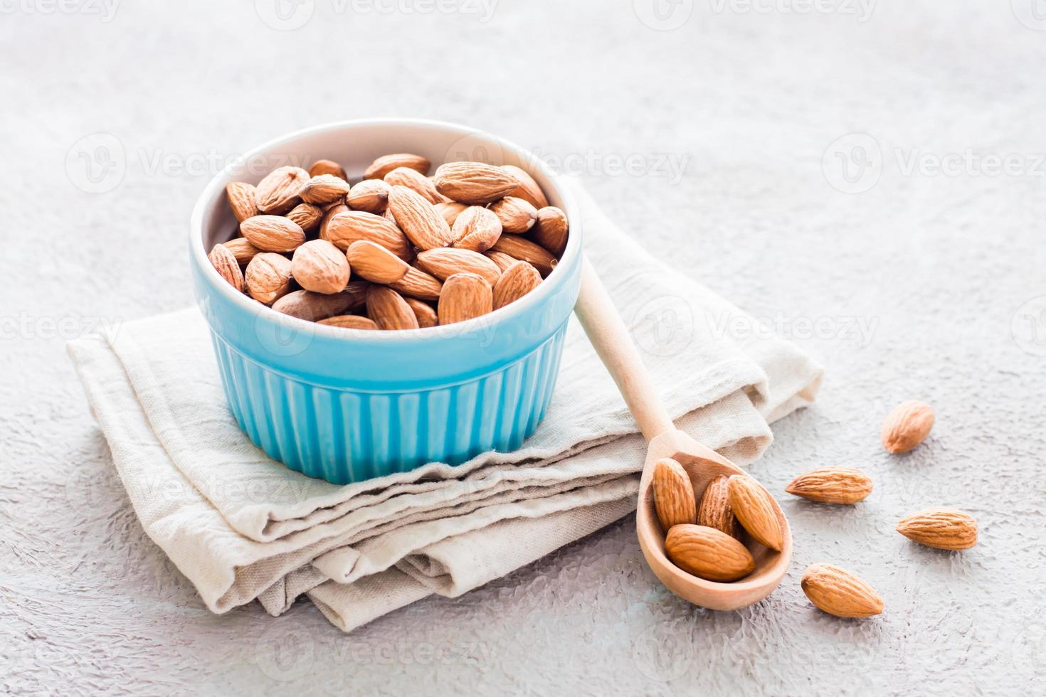 Fresh peeled almonds in a wooden spoon and in a bowl nearby on a light background. A source of vitamins and oils. Organic food. Copy space photo