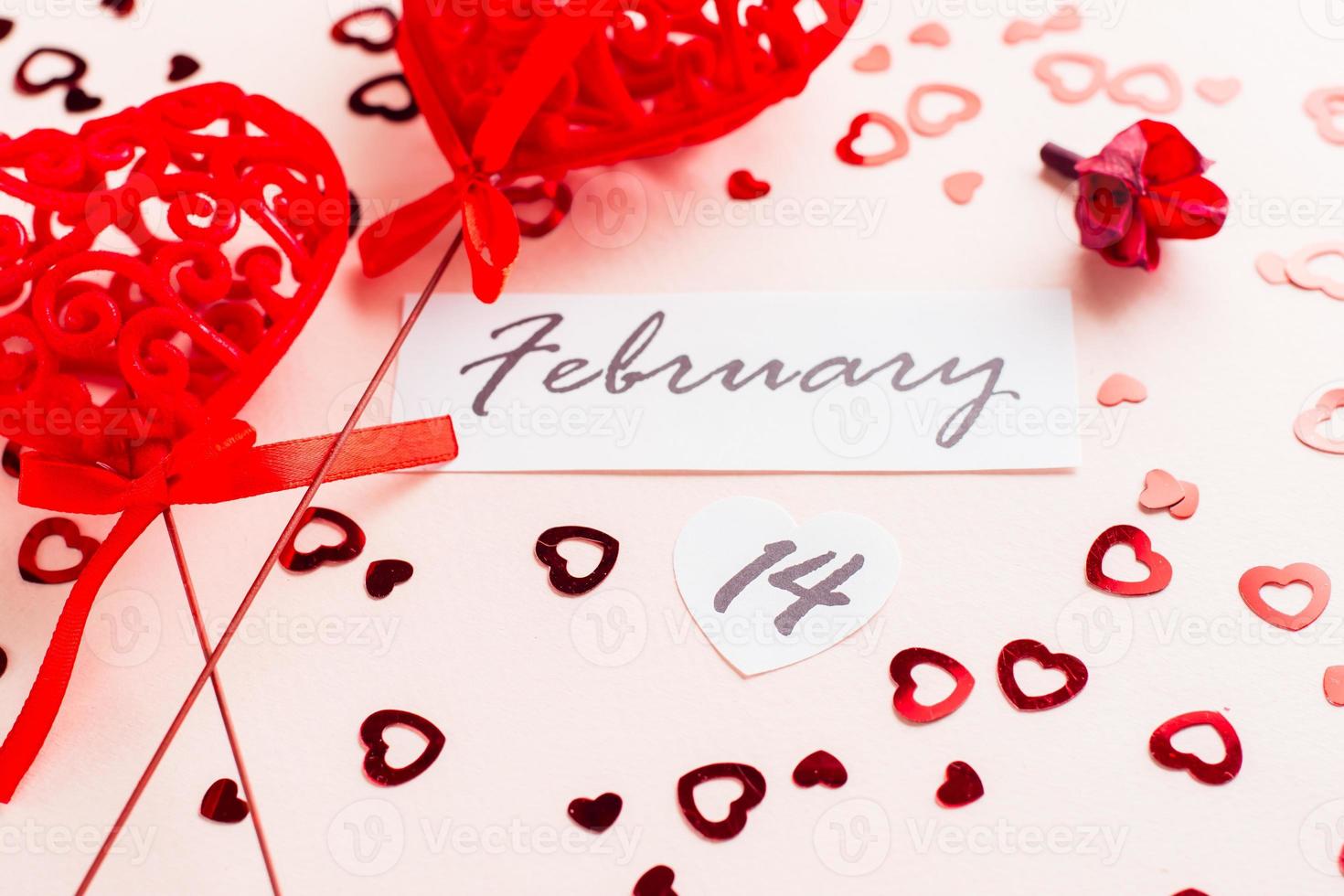 Valentine's Day. Date of February 14 and two curly red hearts on a pink background strewn with hearts. Close-up photo