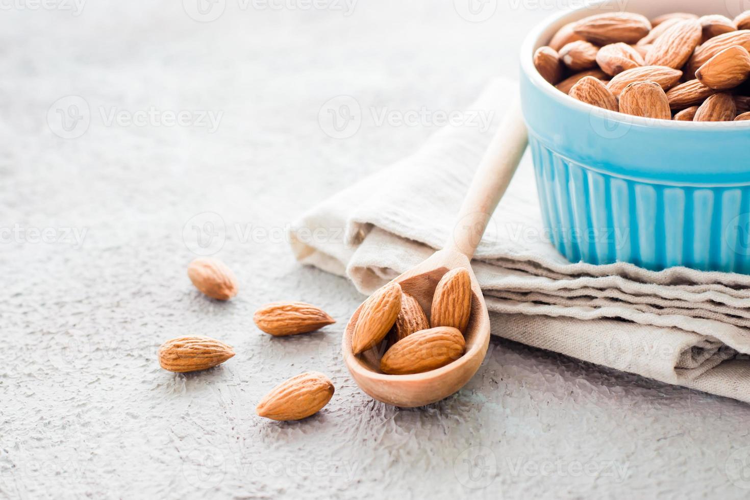 Fresh peeled almonds in a wooden spoon and in a bowl nearby on a light background. A source of vitamins and oils. Organic food. Close-up photo