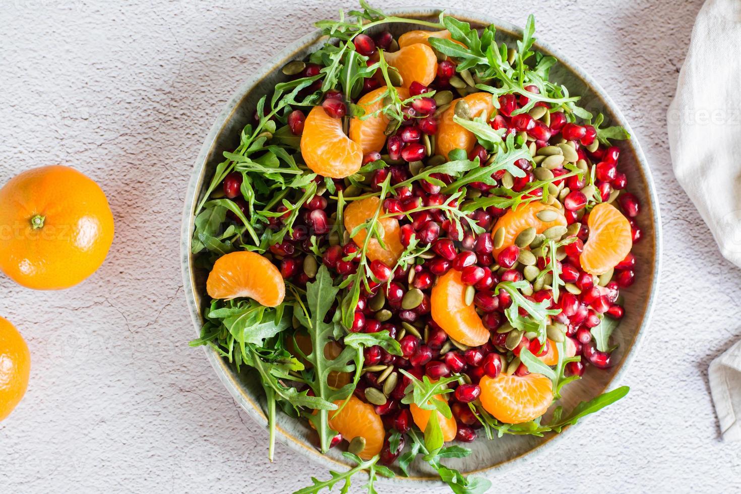 Fruit vitamin salad of pomegranate, tangerine, arugula and pumpkin seeds in a plate on the table. Organic vegetarian food.  Top view. Close-up photo