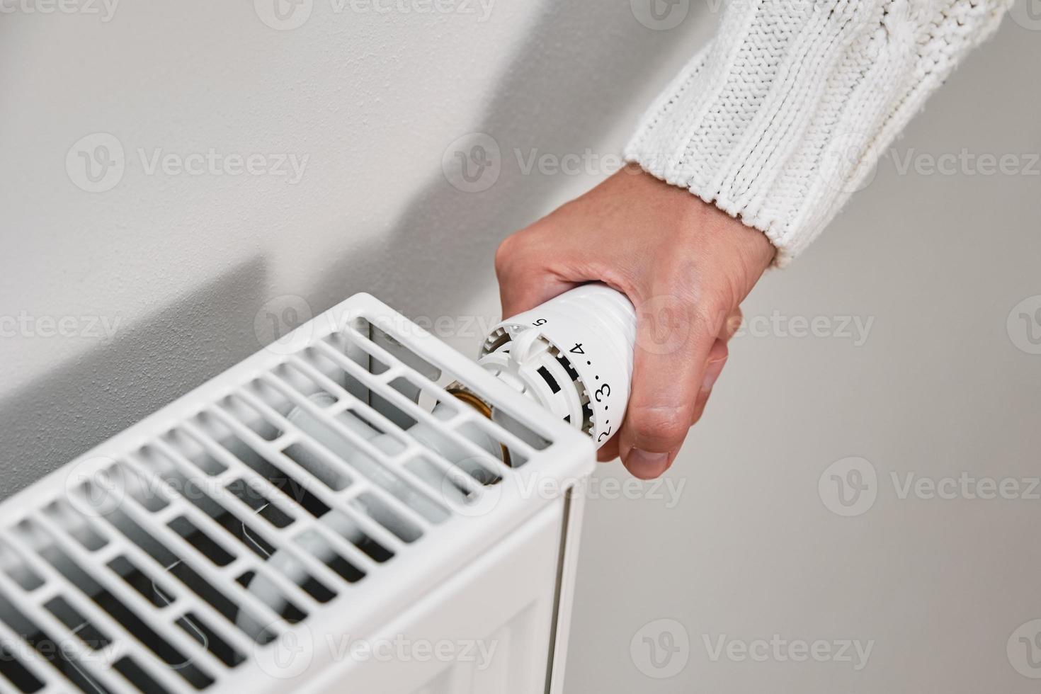 mujer en calentar suéter ajustando temperatura en calefacción radiador foto