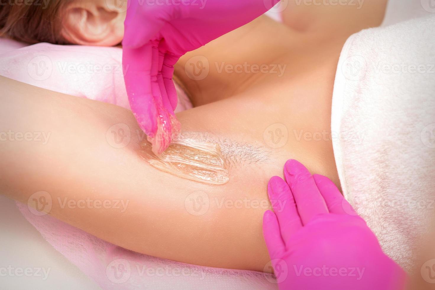 Beautician waxing young female armpit photo