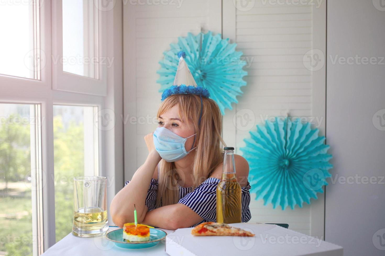 A sad man celebrates a birthday alone in a medical mask and looks boredly out the window. photo