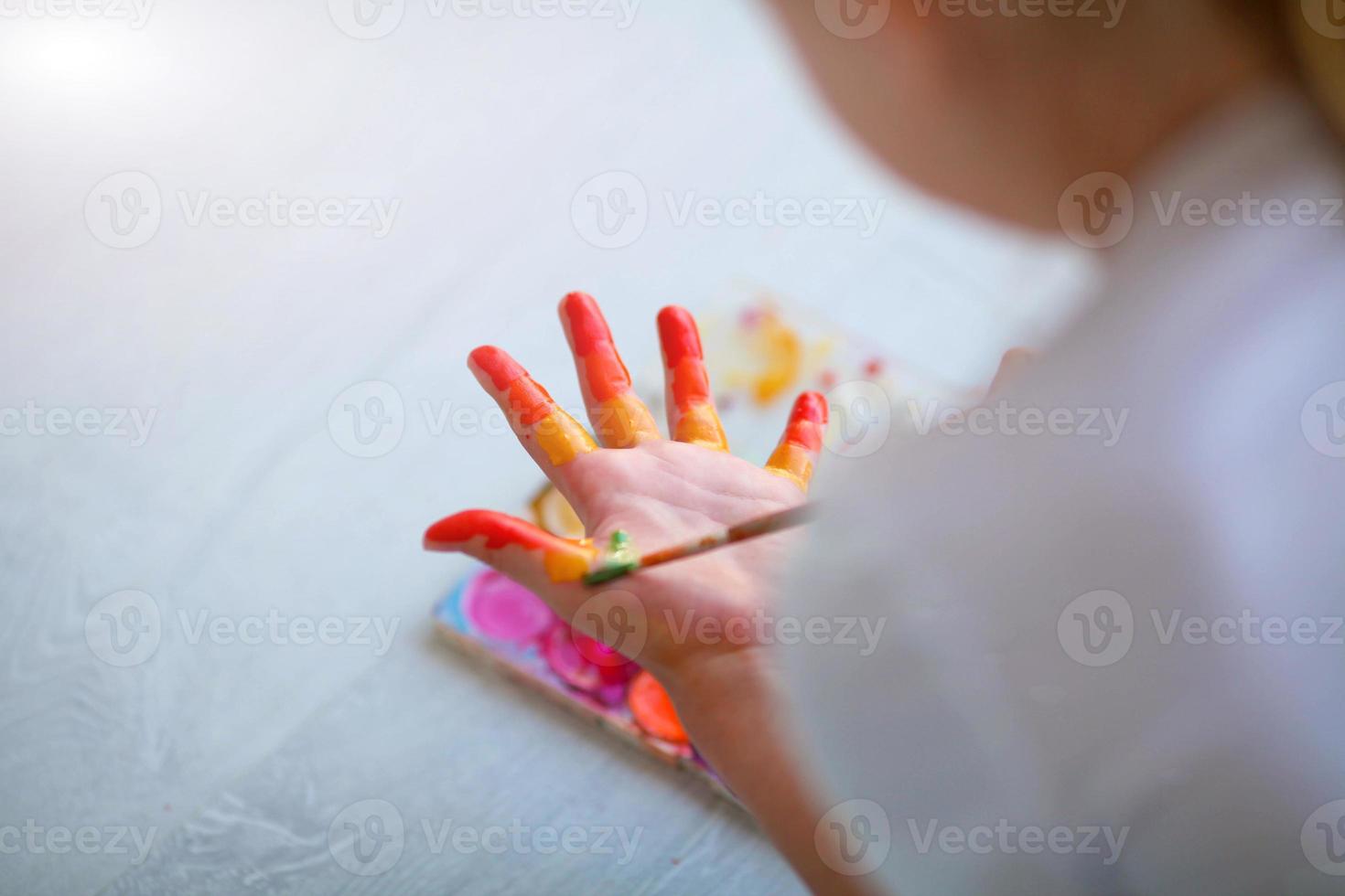 Child girl sitting on the floor and paints the palm of his hand. Quarantine. photo