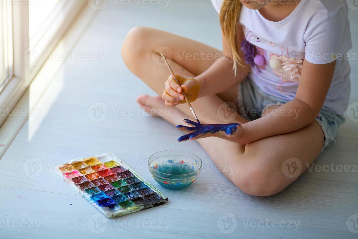 Child girl sitting on the floor and paints the palm of his hand. Quarantine. photo