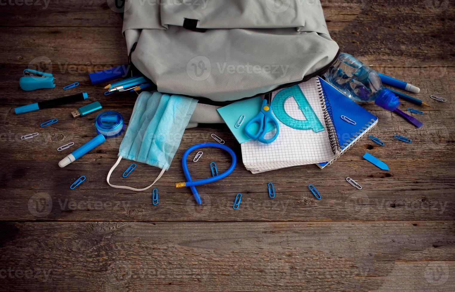 Backpack with school supplies and medical mask on wooden background. View from above. Copy space. Back to school after quarantine concept. photo