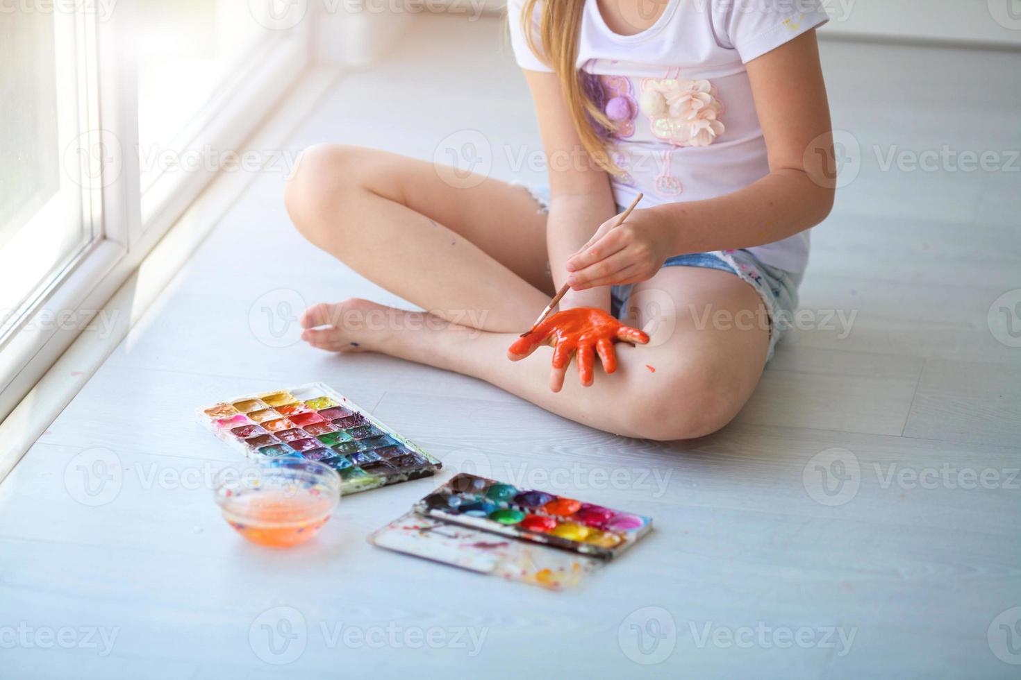 The child sits on the floor and paints his palm with orange paint. photo