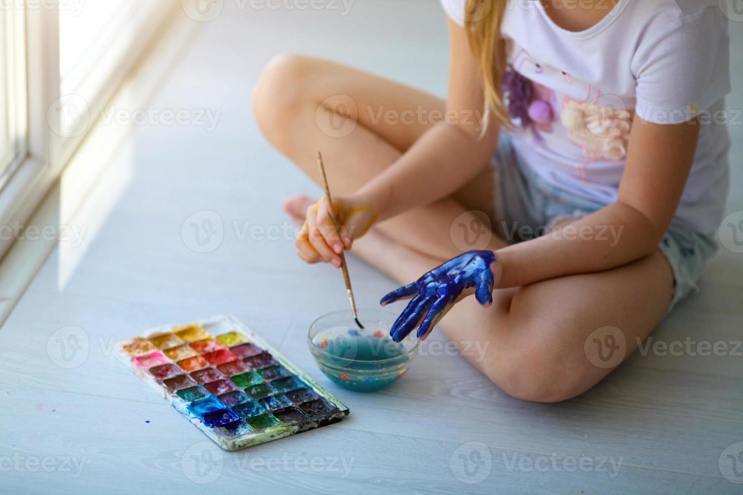 Child girl sitting on the floor and paints the palm of his hand. Quarantine. photo