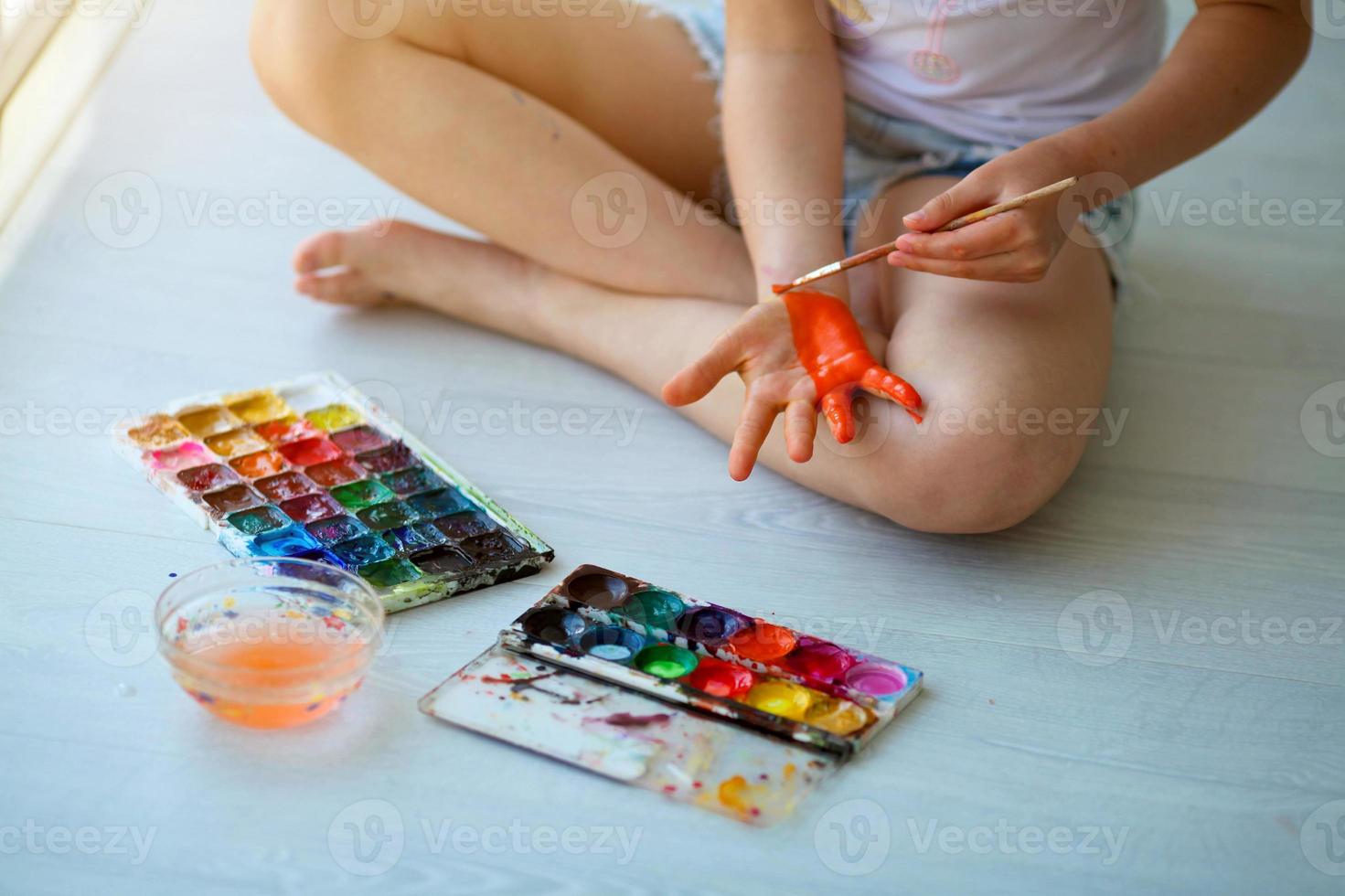 Child girl sitting on the floor and paints the palm of his hand. photo