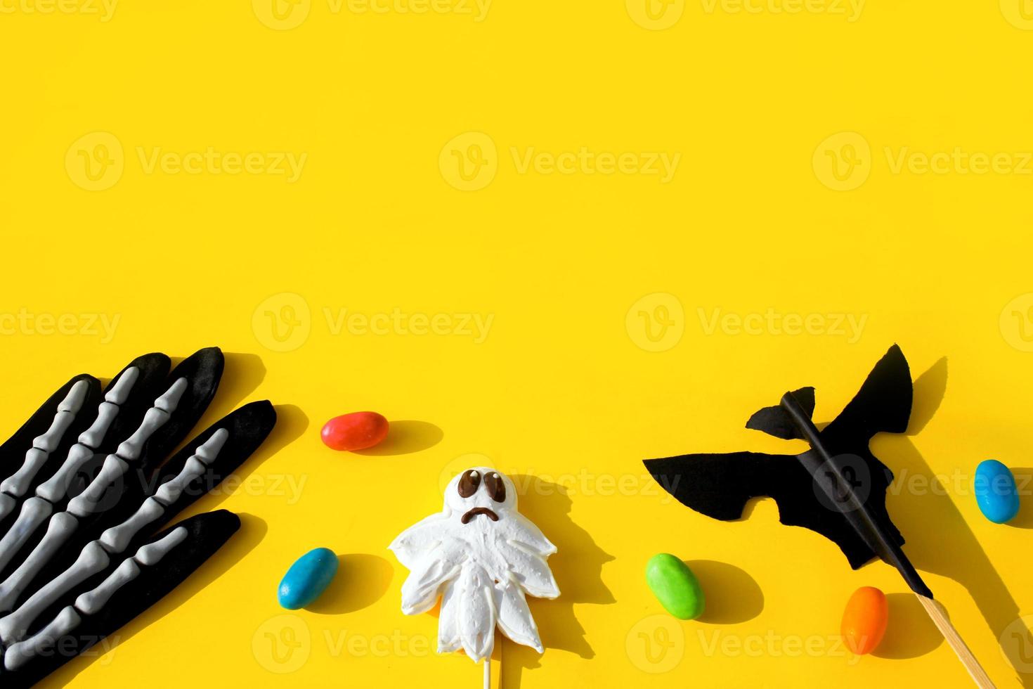 Top view of Halloween crafts, candy ghost, paper bat and skeleton glove on yellow background . photo