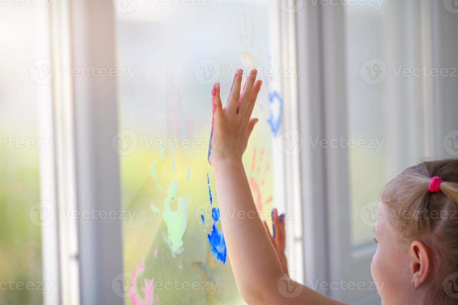 Children girl draw with palms on the window. Painted hands leave a mark on the glass. Quarantine. Stay home. photo