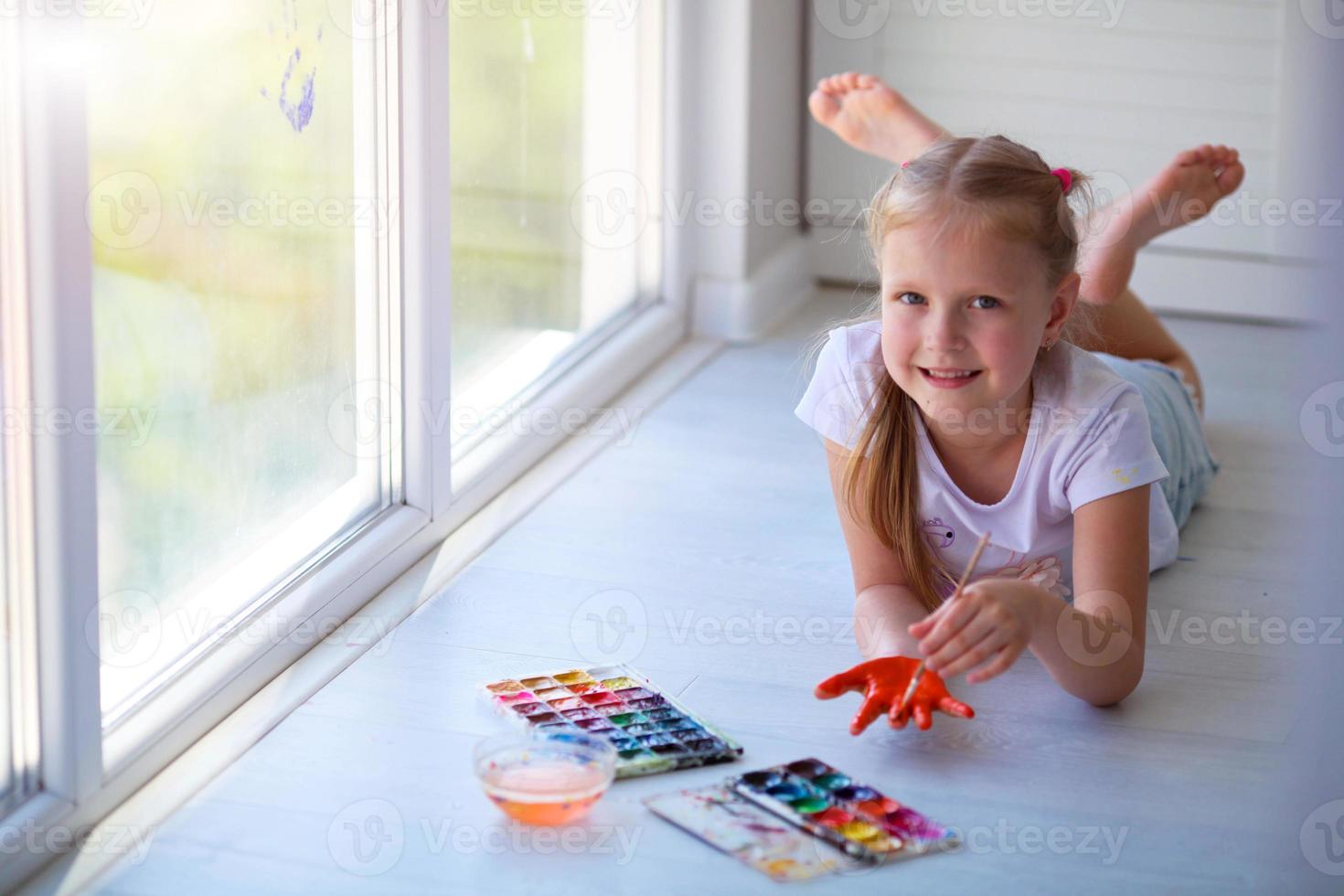 Child girl lies on the floor and paints a palm with paints. photo