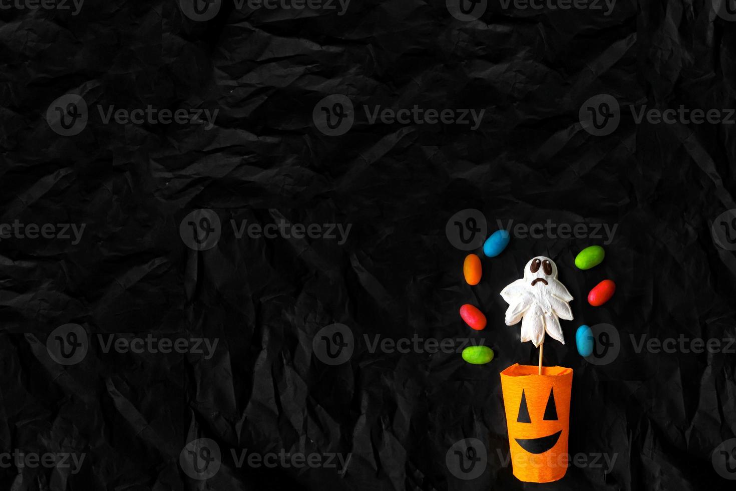 Handmade paper cup in the form of a pumpkin, a confession and jelly candies on a black crumpled background. Top view . photo