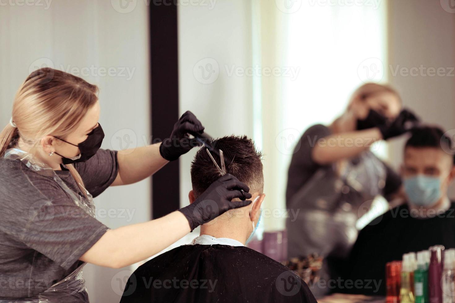 Close up hairdresser with security measures for Covid-19, cuts a man  social distance, cutting hair with a medical mask photo