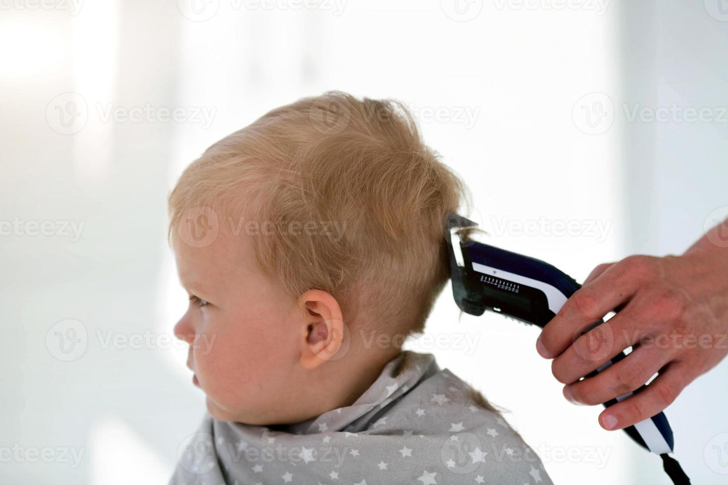 hembra manos cortar un niño con un pelo clíper en un peluquero. el primero Corte de pelo. foto