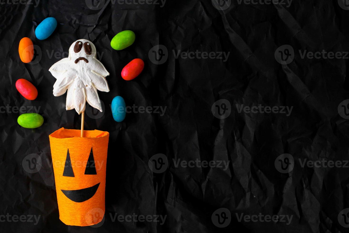 Handmade paper cup in the form of a pumpkin, a confession and jelly candies on a black crumpled background. Top view . photo