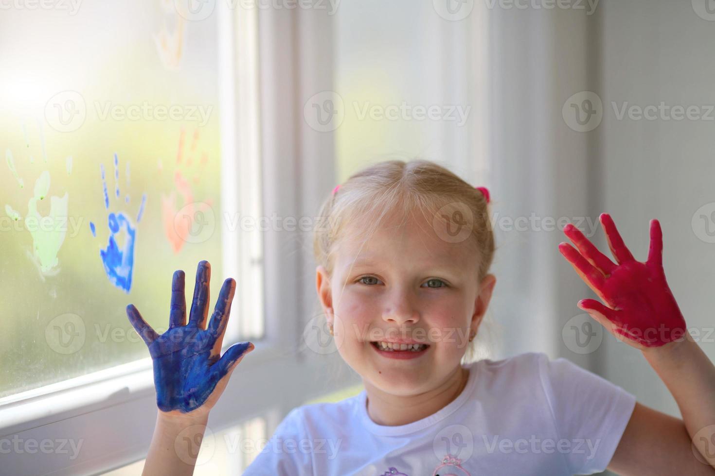 Children girl draw with palms on the window. Painted hands leave a mark on the glass. Quarantine. Stay home. photo