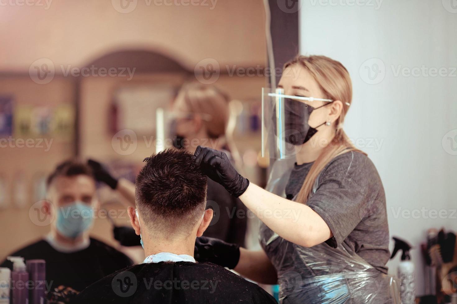 Hairdresser with security measures for Covid-19, cuts a man in a medicine mask, social distance, cutting hair with a medical mask, eye mask and rubber gloves. photo