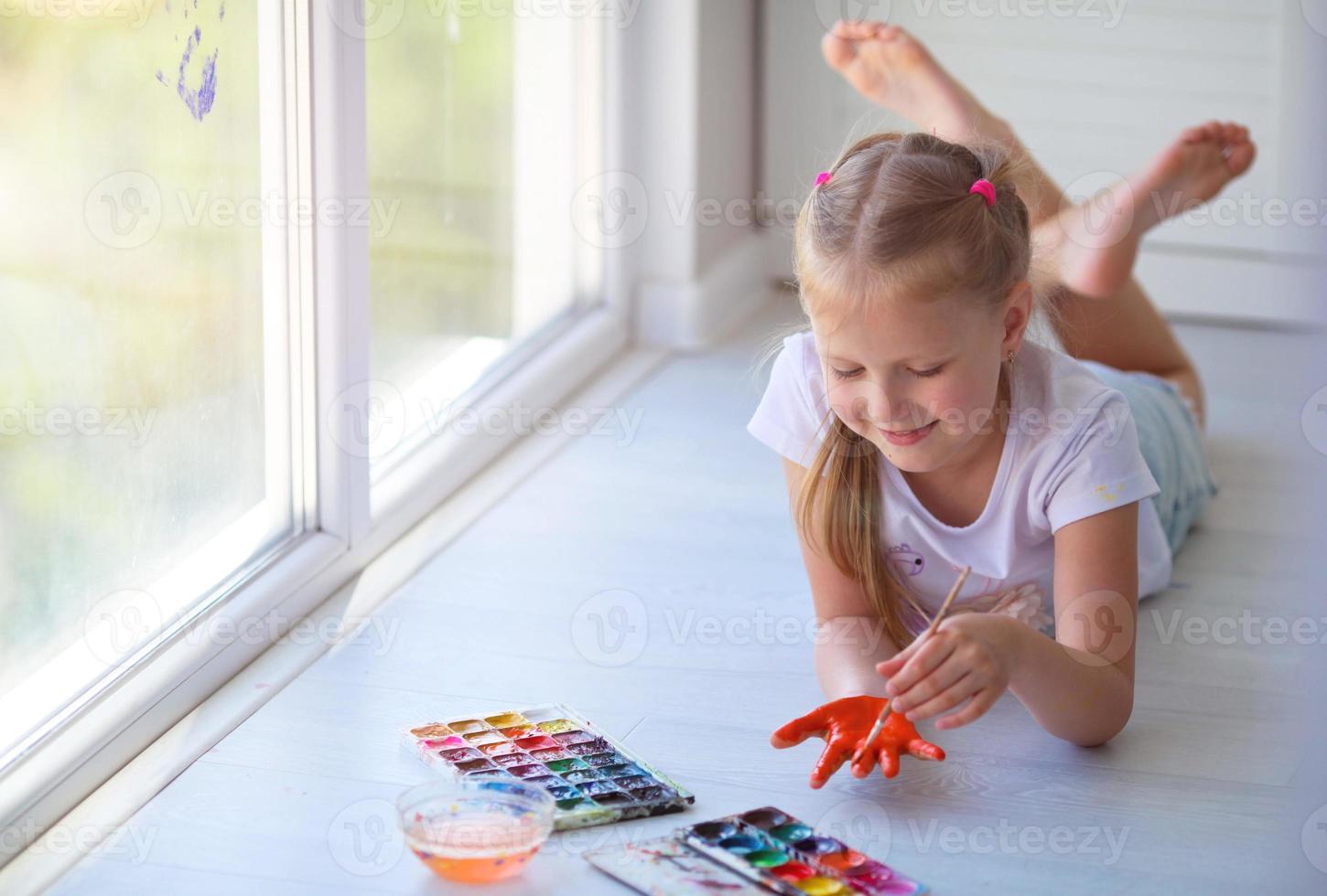 Child girl lies on the floor and paints a palm with paints. photo