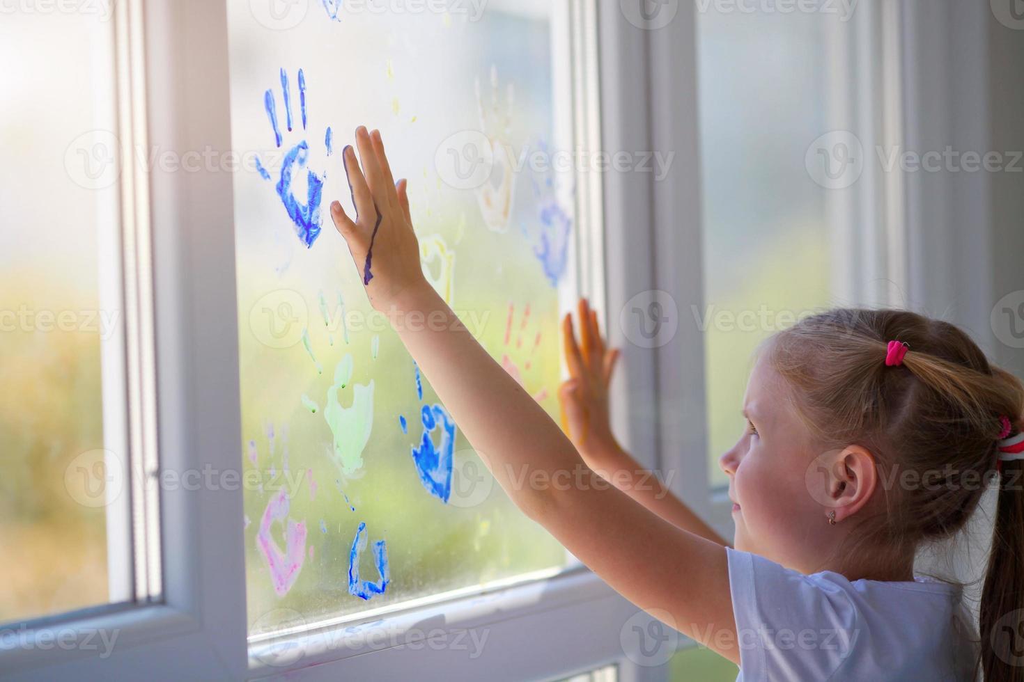 Children girl draw with palms on the window. Painted hands leave a mark on the glass. Quarantine. Stay home. photo