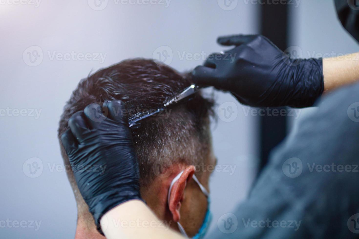 A hairdresser with security measures for Covid-19, holds scissors in his hands a man, social distance, cutting hair with rubber gloves in a beauty salon photo