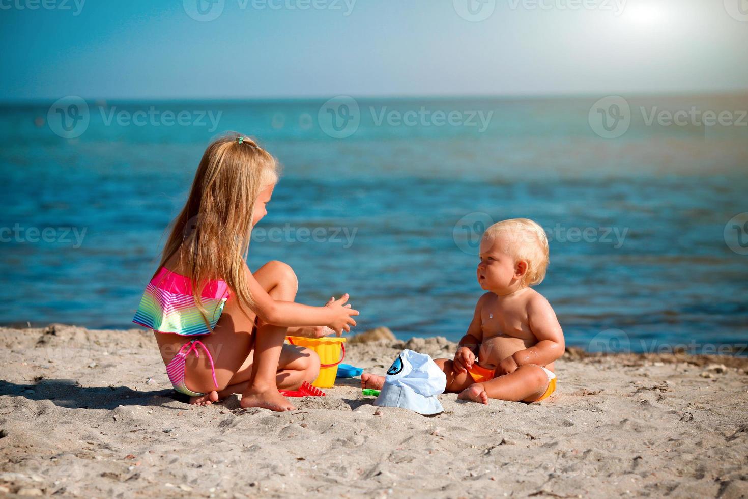 niños jugar en el playa. verano agua divertido para el familia. chico y niña con juguete cubos y un pala en el costa. relajarse en el Oceano con un bebé y niño pequeño. foto