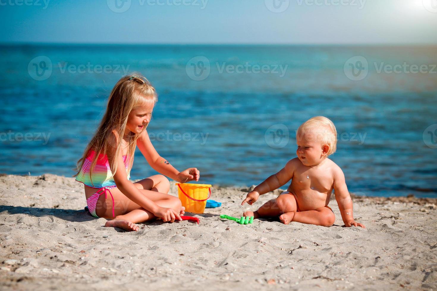 Children play on the beach. Summer water fun for the family. Boy and girl with toy buckets and a shovel on the seashore. photo