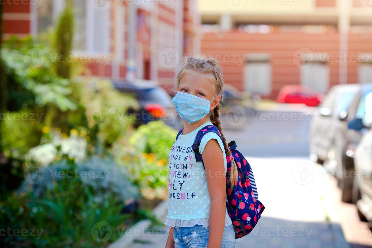 concepto de coronavirus COVID-19. Chica de escuela vistiendo médico cara máscara a salud proteccion desde influenza virus. espalda a colegio en cuarentena. foto