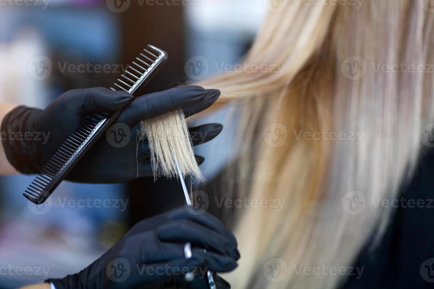 A hairdresser in rubber gloves holds a pair of scissors and a comb. Woman getting a new haircut. photo