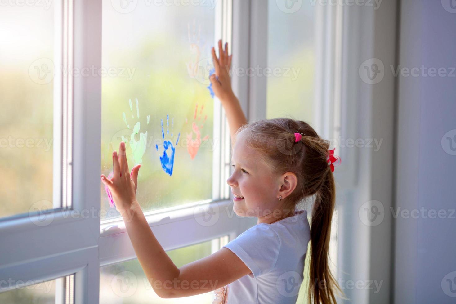 Children girl draw with palms on the window. Painted hands leave a mark on the glass. Quarantine. Stay home. photo