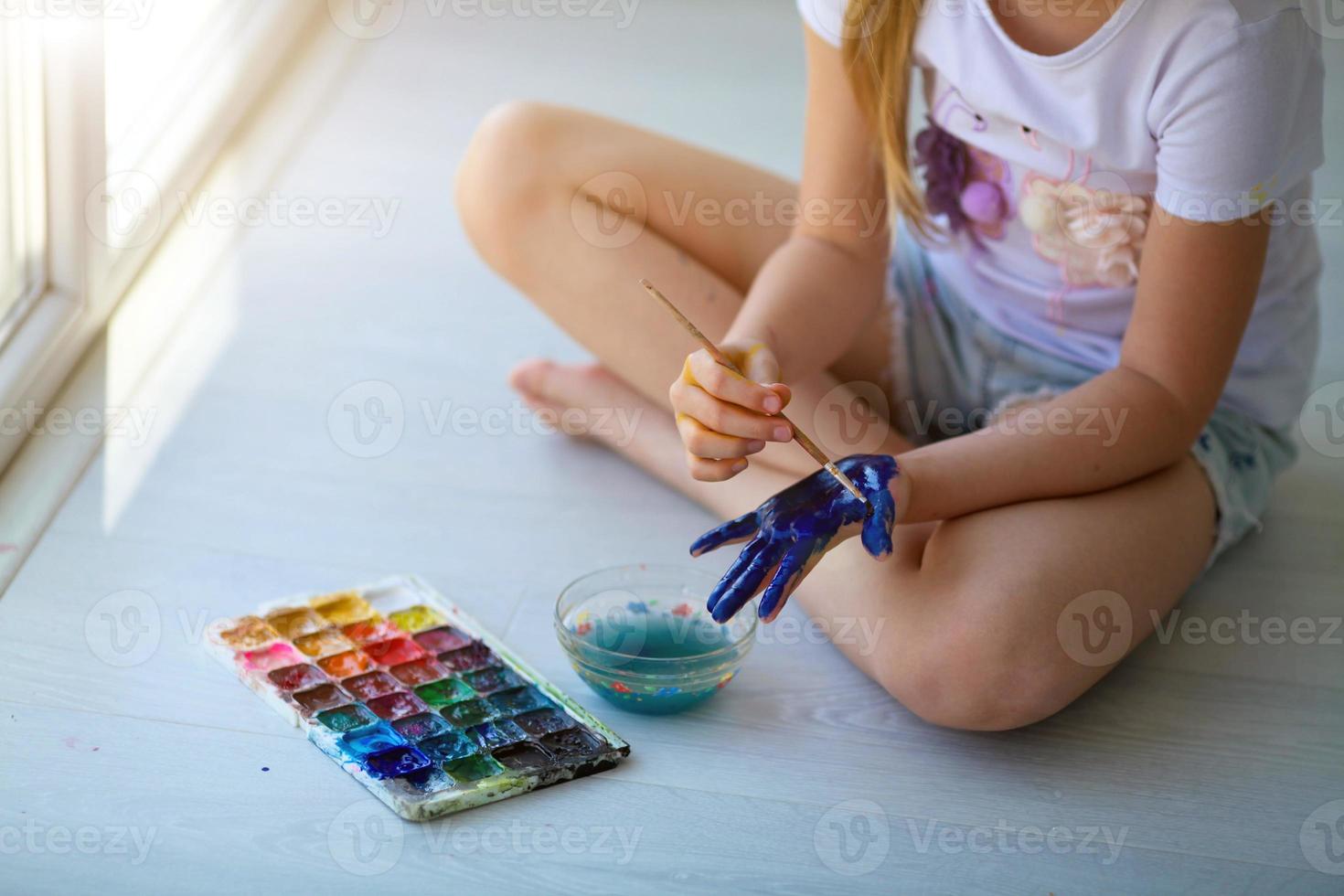 Child girl sitting on the floor and paints the palm of his hand. Quarantine. photo