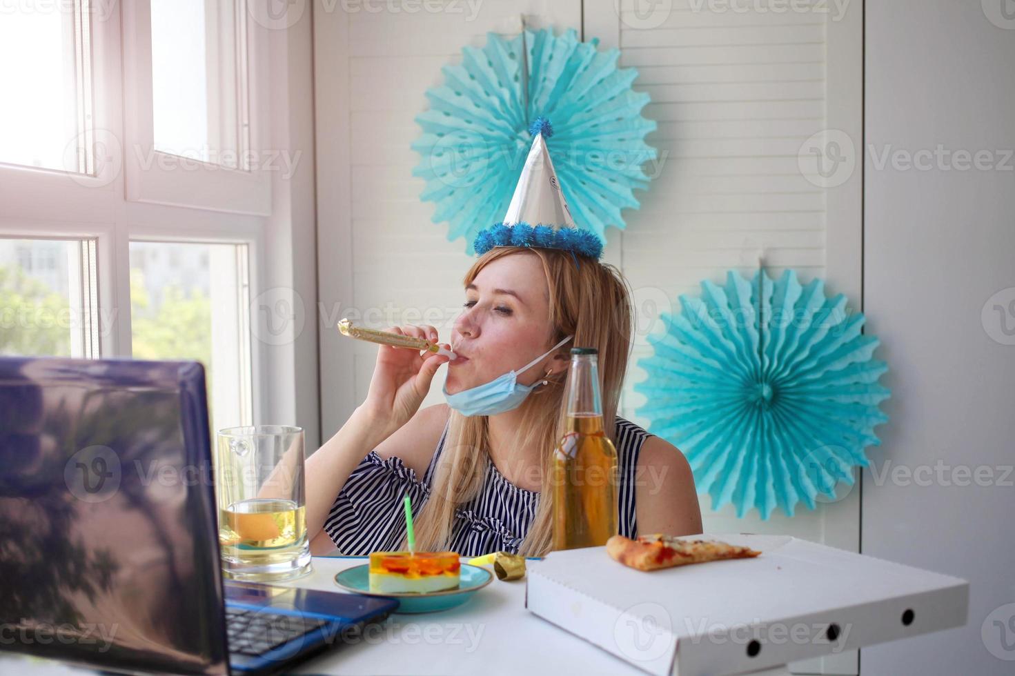 A woman in a medical mask sits in front of a laptop and blows whistles photo