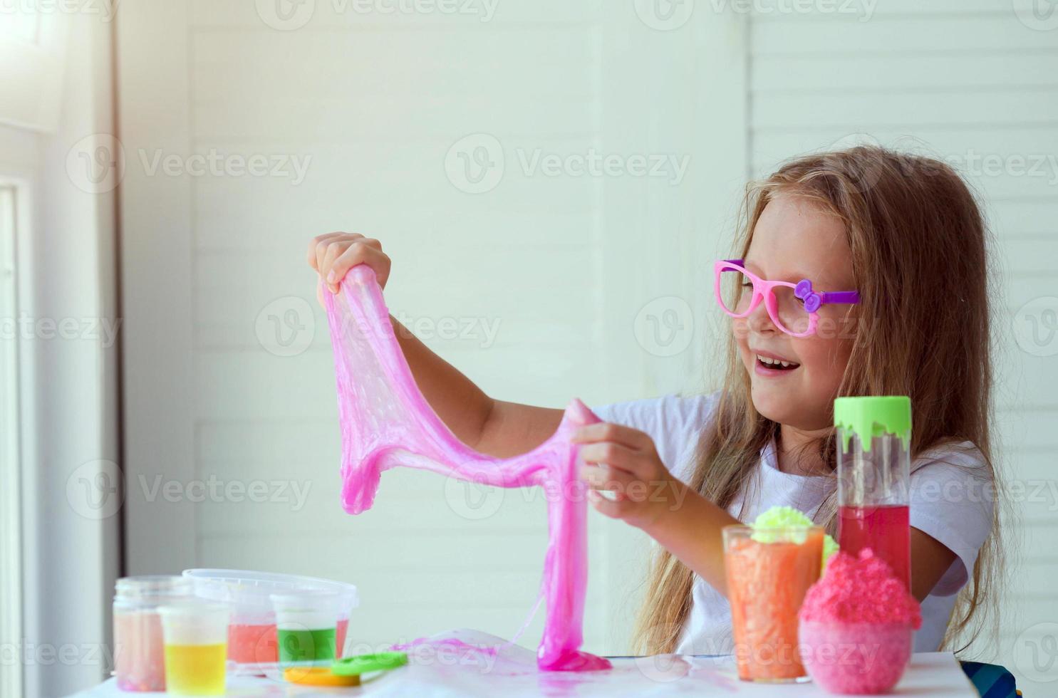 Little girl stretching pink slime to the sides. Kids hands playing slime toy. photo