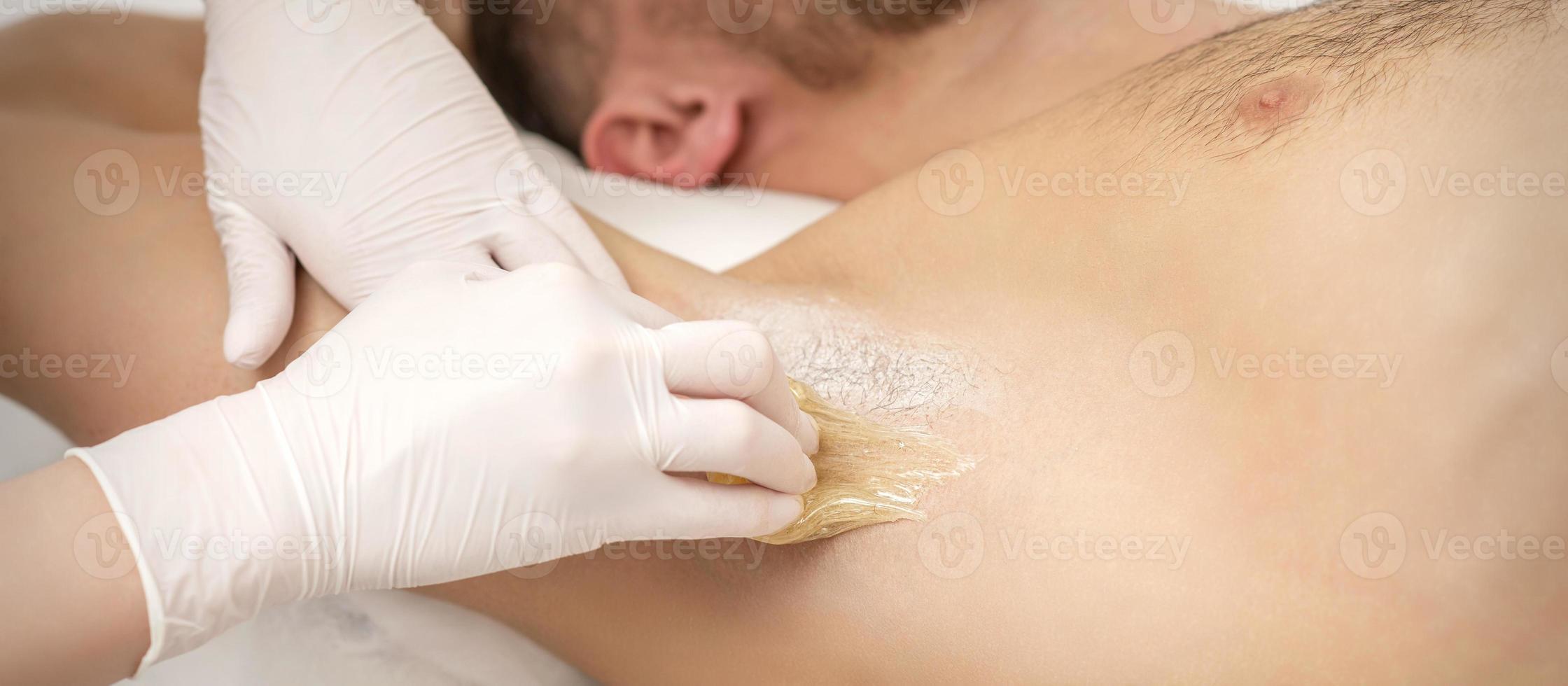 Beautician waxing young male armpit photo